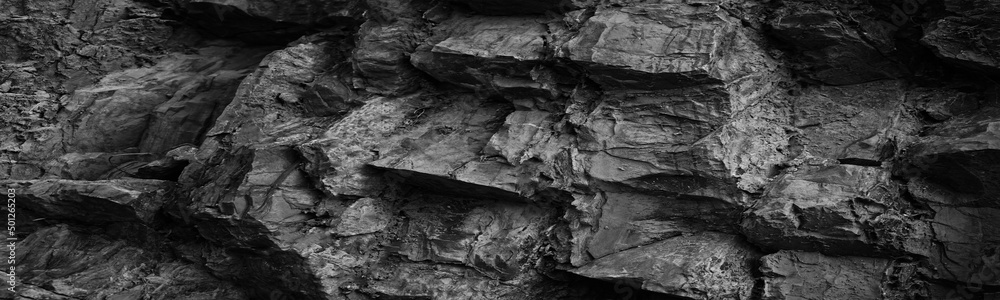 Black white rock texture. Rough mountain surface. Close-up. Volumetric stone background with space for design. Dark gray grunge backdrop. Wide banner. Panoramic.