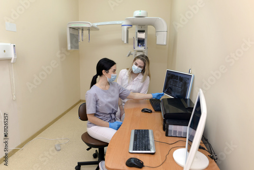a female dentist and a girl patient are looking at an x-ray of the jaw and teeth on a digital screen in a modern clinic.