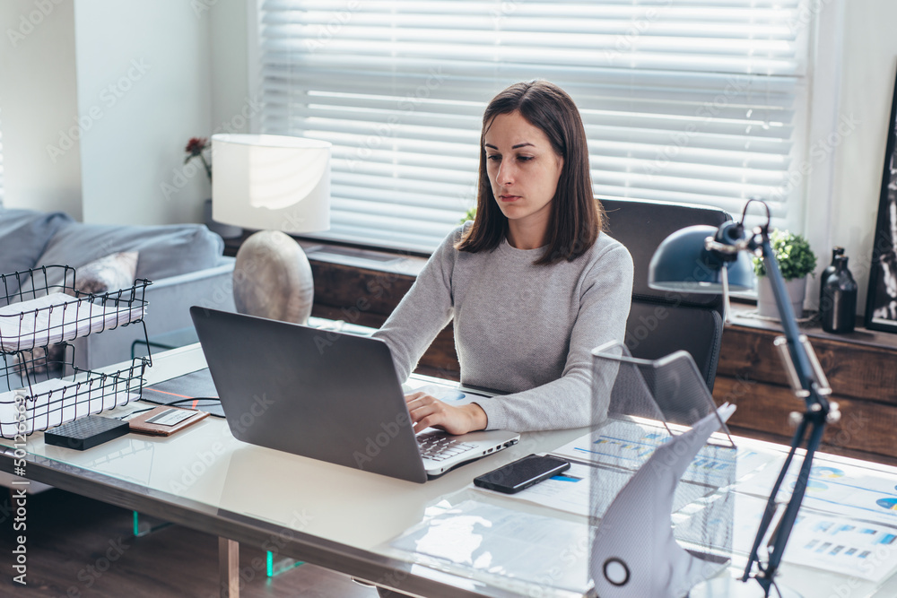 Side view of young woman working in office sitting and using laptop Side view of young woman working in office sitting and using laptop