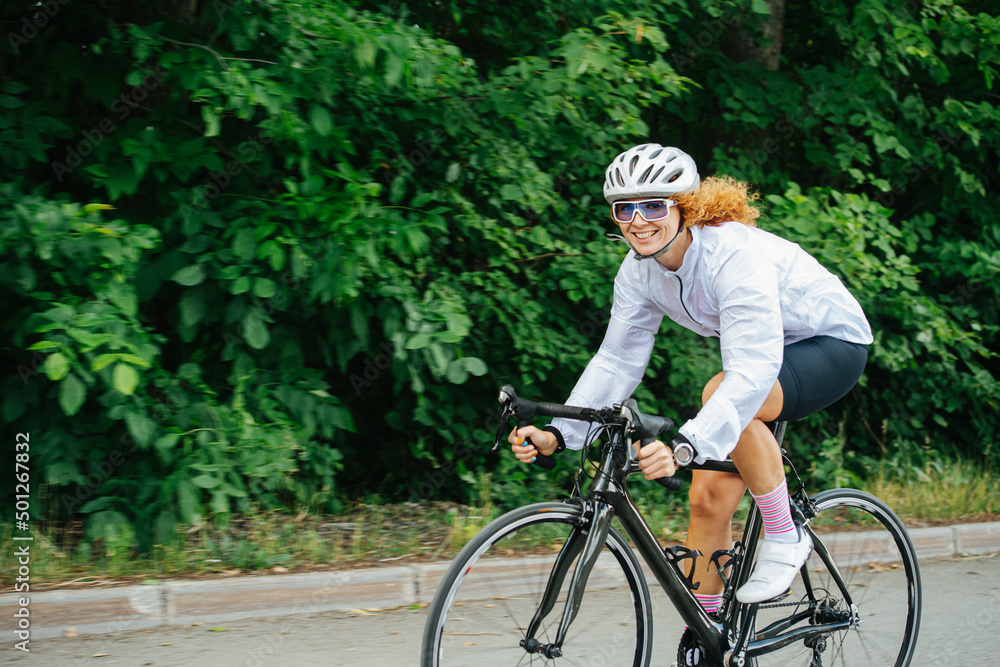 Obraz premium Quirky woman with curly hair in a helmet riding street racing bike on a road
