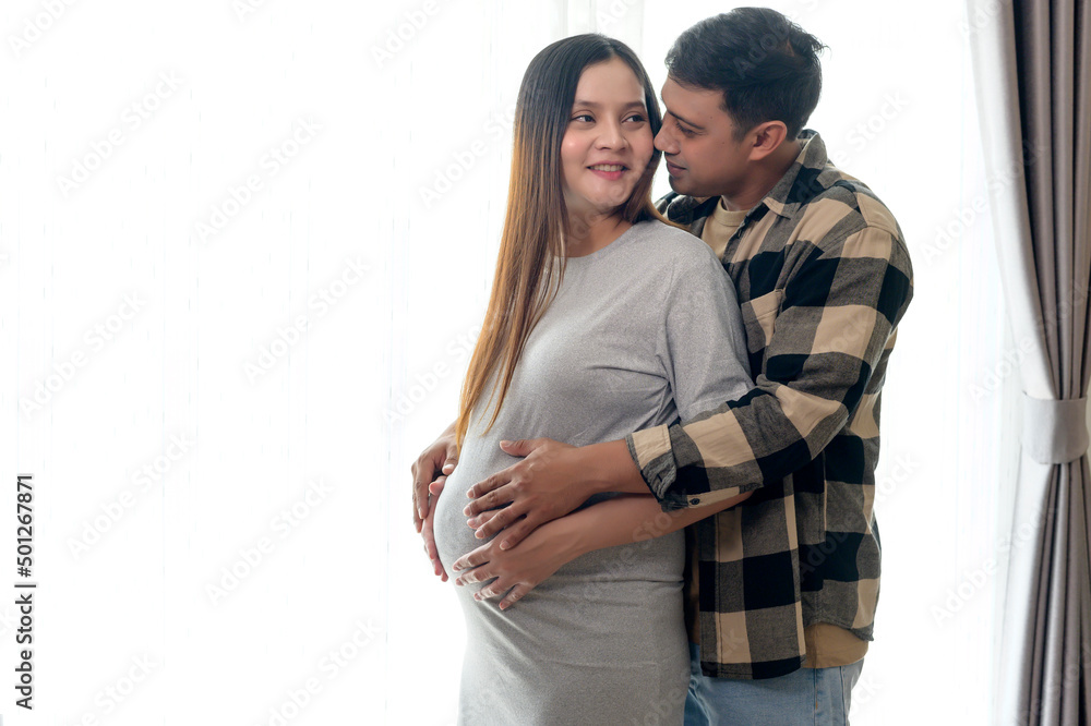 Young pregnant woman with husband embracing and expecting a baby at home Young pregnant woman with husband embracing and expecting a baby at home