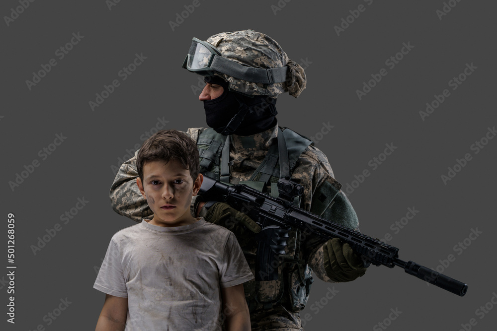 Soldier protecting little kid. Special force army man and young boy against gray background. Soldier protecting little kid. Special force army man and young boy against gray background.