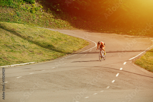 Strong muscular man riding his racing bike on a mountain road through hills