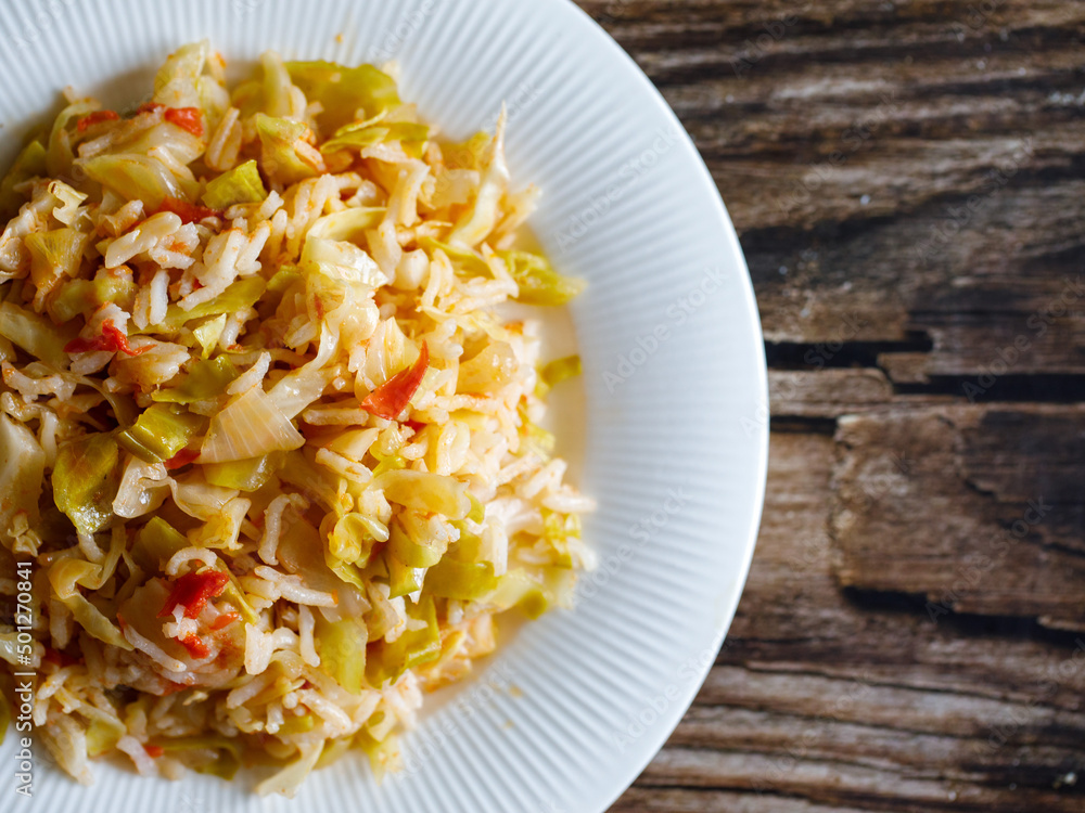 Traditional homemade Mediterranean Crete cuisine rice with vegetables cabbage, onion and tomato on white plate on old wooden table. Vegetarian healthy lunch or dinner idea. Top view