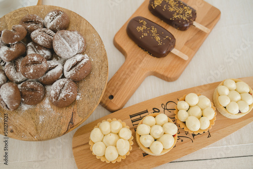 Coffee cookies, tartlet with berry jam and protein cream, ice cream in chocolate  on a wooden tray on a white tablecloth.