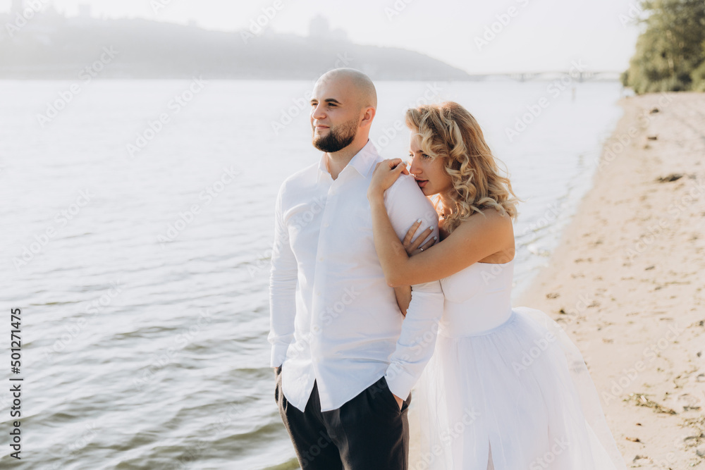 Wedding photosession at sunset of a beautiful couple, the bride in a white dress, and the groom in a white shirt and black trousers Wedding photosession at sunset of a beautiful couple, the bride in a white dress, and the groom in a white shirt and black trousers