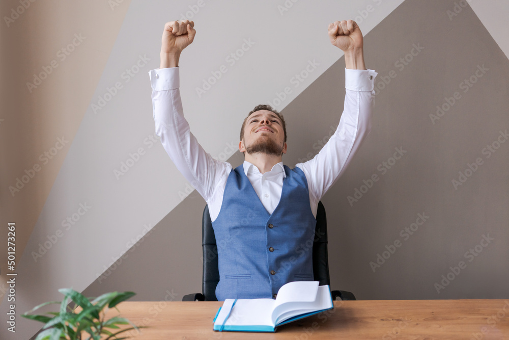 Happy businessman beard man in suit looking smiling excited with good news, lucky successful winner man sitting at office desk raising hand in winner gesture, celebrating business success in office Happy businessman beard man in suit looking smiling excited with good news, lucky successful winner man sitting at office desk raising hand in winner gesture, celebrating business success in office