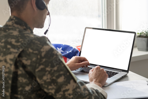 military man gesturing in office near laptop with blank screen, usa flag.