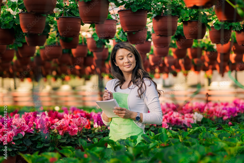 A beautiful flower greenhouse owner uses a notebook to write down all the flowers she needs to deliver.
