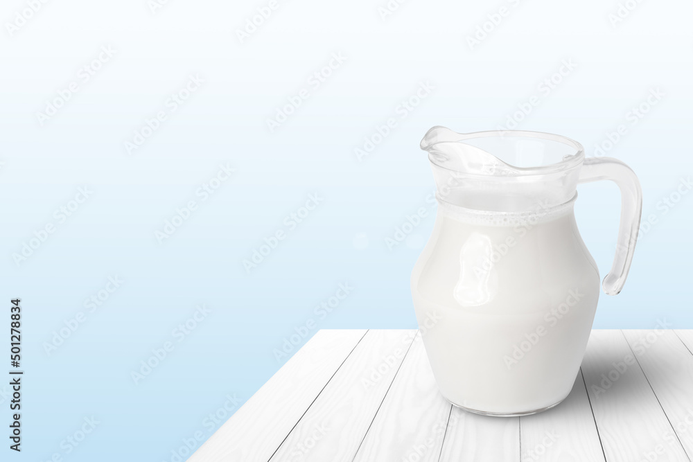 Glass jug of fresh milk on white wooden table with blue background. Copy space. Glass jug of fresh milk on white wooden table with blue background. Copy space.