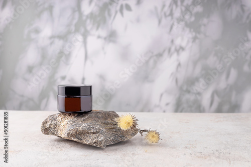  jar of cream, a stone and a dried flower on a background with abstract shadows, selective focus