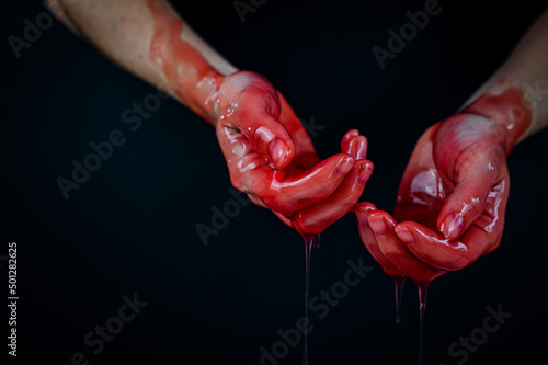 Women's hands in a viscous red liquid similar to blood.
