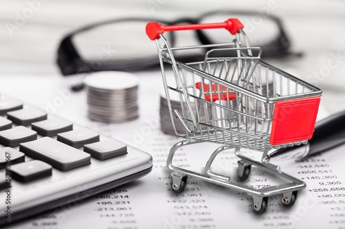 Shopping cart and man working on calculator with financial document. Financial crisis concept.