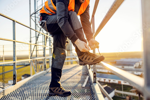 Fotografia A heavy industry worker tying shoelace on his work shoes while standing on height
