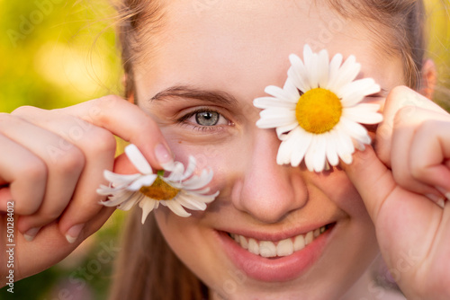 A beautiful young girl smiles at the camera and holds flowers chamomile in her hands
