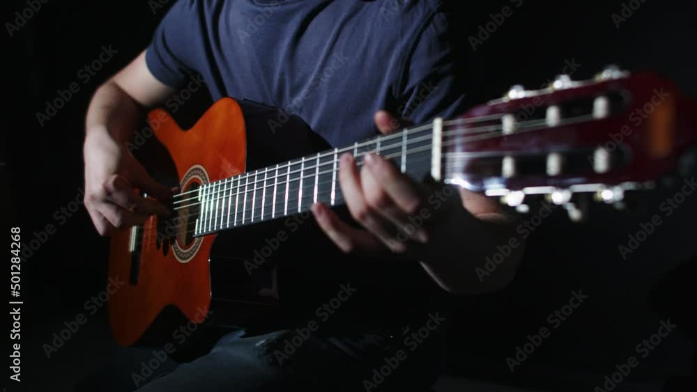 Male musician plays song on guitar sitting at chair in studio, closeup, front view. Man musician plays on guitar. Music concept Male musician plays song on guitar sitting at chair in studio, closeup, front view. Man musician plays on guitar. Music concept