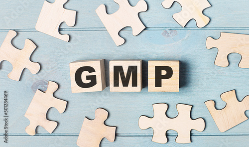 Blank puzzles and wooden cubes with the text GMP Good Manufacturing Practice lie on a light blue background.