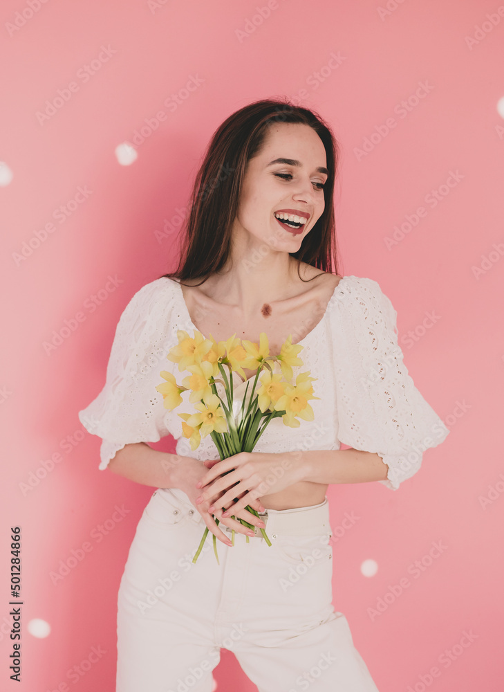Woman of model appearance holds yellow flowers in her hands and smiles on a pink background
Woman of model appearance holds yellow flowers in her hands and smiles on a pink background