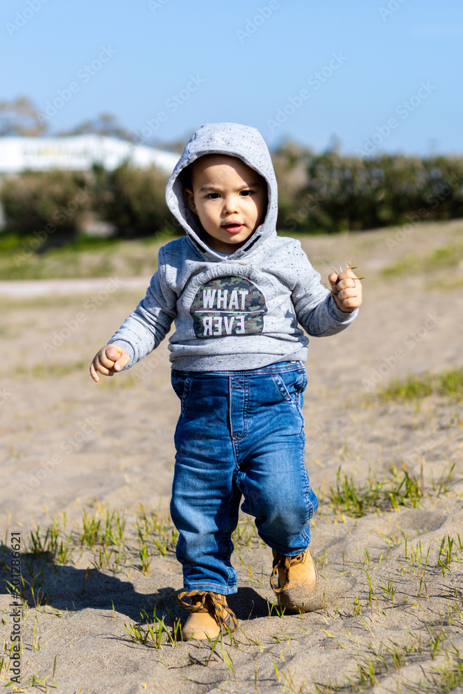 Sweet baby boy in hoodie and jeans walking and playing in the sand. Activity with toddler. Sweet baby boy in hoodie and jeans walking and playing in the sand. Activity with toddler.