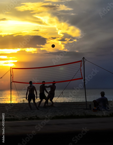 Silhouette of men playing beach volleyball at sunset in summer