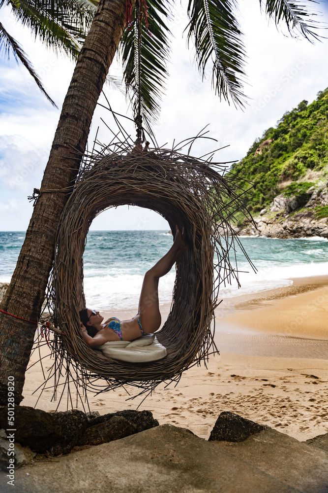 Fototapeta premium Young beautiful female model pose on the swing nest at Nui Beach Phuket Thailand