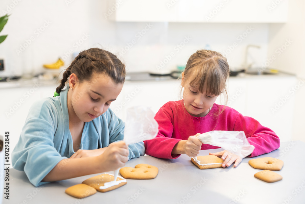 two little sisters decorating homemade cookies in the kitchen at home. two little sisters decorating homemade cookies in the kitchen at home.