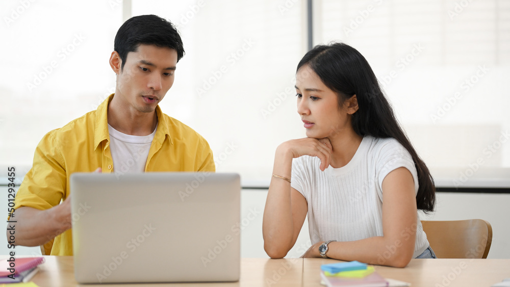 Male software engineer fixing the problems on laptop computer for female officer Male software engineer fixing the problems on laptop computer for female officer