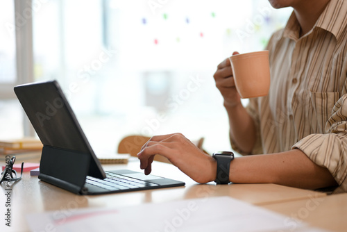 A male officer or businessman having coffee while typing on tablet