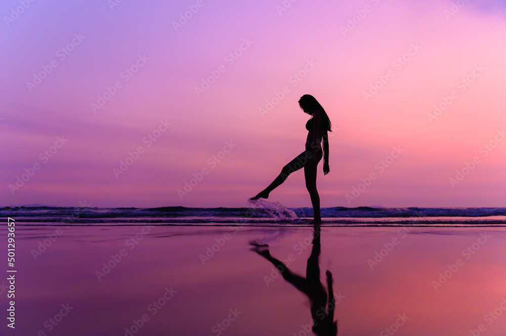 Silhouettte photo of young beautiful Asian woman with bikini walking along beautiful beach at twilight sunset time. Happy or Freedom woman concept.