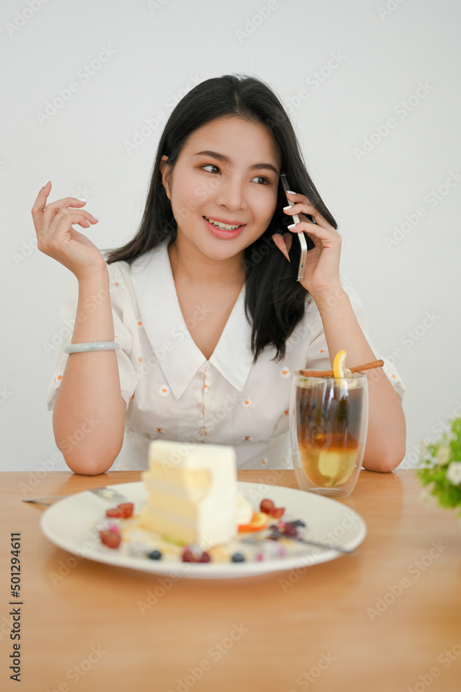 Woman sitting in the cafe, talking on smartphone while eating cake. Woman sitting in the cafe, talking on smartphone while eating cake.