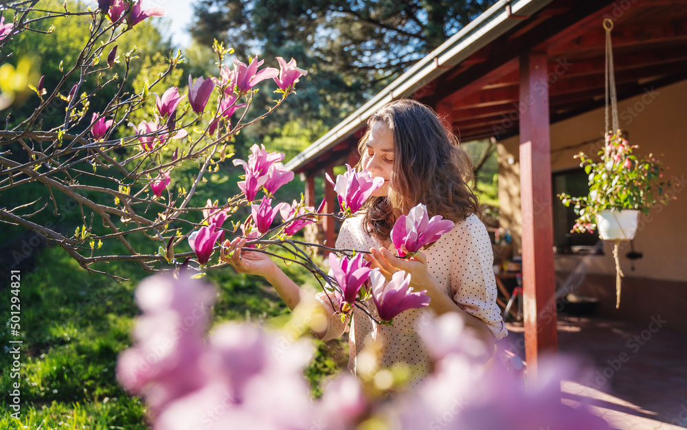 Young beautiful woman enjoying the spring of her home in the garden near a blooming magnolia tree inhaling the aroma of flowers