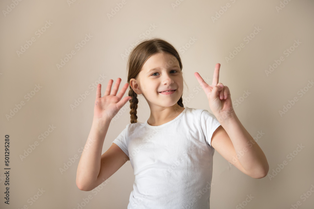 A child in a white T-shirt shows numbers on his fingers, beige background A child in a white T-shirt shows numbers on his fingers, beige background