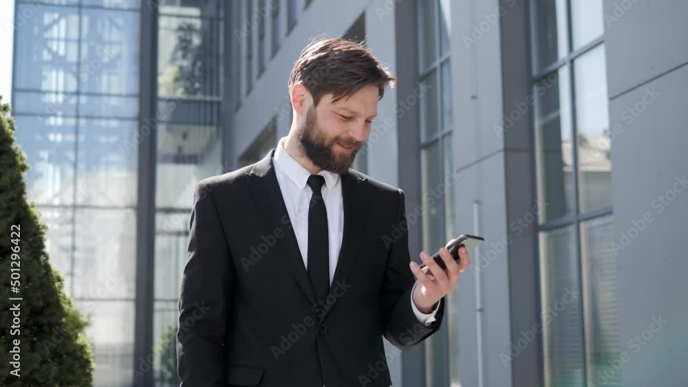 Handsome happy young businessman in tie using smartphone texting message reading sms at street. Male model in business style tapping and scrolling on mobile phone. Outdoors. Successful people. Handsome happy young businessman in tie using smartphone texting message reading sms at street. Male model in business style tapping and scrolling on mobile phone. Outdoors. Successful people.