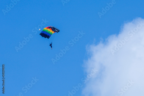 Pilot is paragliding with rainbow glide to promote lgbtq in gender equality in the extreme sport with bright blue sky and white fluffy cloud