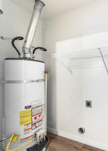 Vertical Empty white laundry room with water heater tank and wall mounted wire shelf