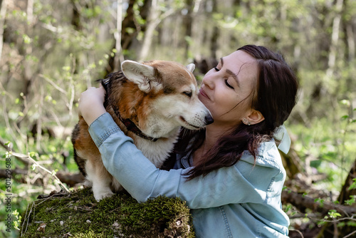 a cute young girl gently hugs a corgi dog in the spring forest