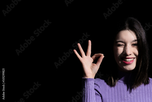 brunette woman doing the ok symbol winking an eye on black background