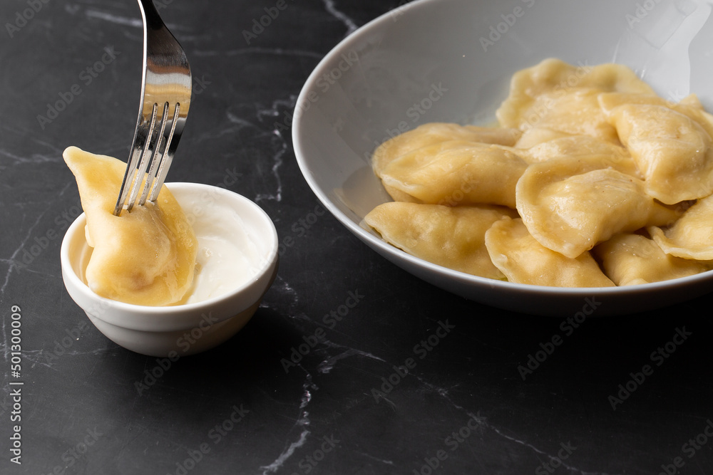 Isolated traditional ukrainian dish vareniki dipping in sour cream on black background. Menu or cook book concept Isolated traditional ukrainian dish vareniki dipping in sour cream on black background. Menu or cook book concept