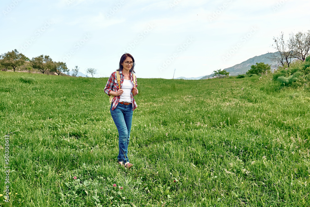 Happy beautiful carefree woman walking on a spring meadow with green grass. Hiking outdoors, unity with nature. Happy beautiful carefree woman walking on a spring meadow with green grass. Hiking outdoors, unity with nature.