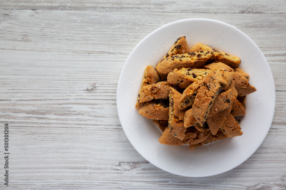 Homemade Italian Cantuccini with Chocolate on a White Plate on a white wooden surface, top view. Crispy Chocolate Cookies. Flat lay, overhead, from above. Copy space. Homemade Italian Cantuccini with Chocolate on a White Plate on a white wooden surface, top view. Crispy Chocolate Cookies. Flat lay, overhead, from above. Copy space.