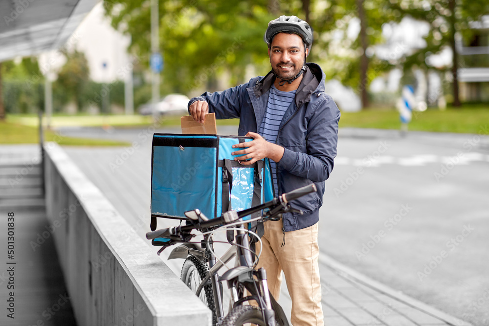 food shipping, profession and people concept - happy smiling indian delivery man with thermal insulated bag and bicycle on city street