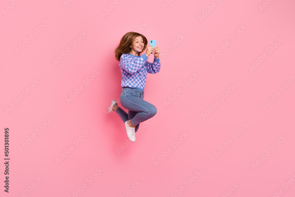 Full length photo of blond little girl jump hold telephone wear sweater jeans footwear isolated on pink background