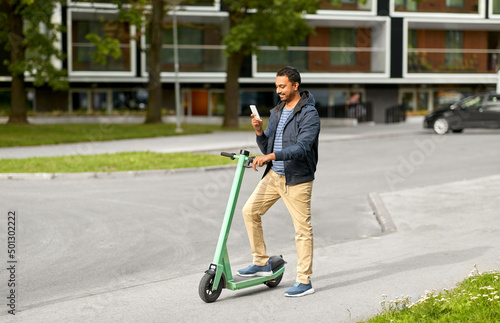 transport, technology and people and concept - happy smiling young man with electric scooter using smartphone on city street
