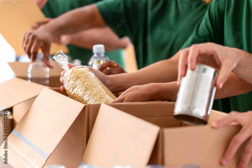 Obraz premium charity, donation and volunteering concept - close up of international group of happy smiling volunteers packing food in boxes at distribution or refugee assistance center