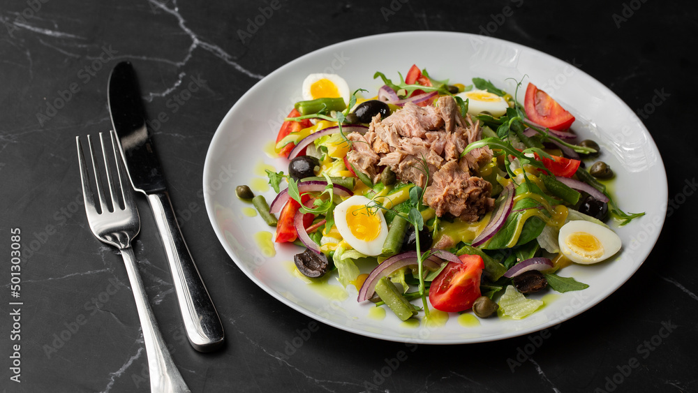 French salad Nicoise with tuna, egg, green beans, tomatoes, olives, lettuce, onions and anchovies on a gray background. Healthy food French salad Nicoise with tuna, egg, green beans, tomatoes, olives, lettuce, onions and anchovies on a gray background. Healthy food