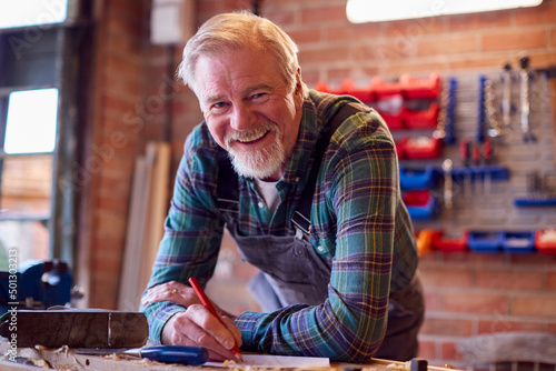 Portrait Of Senior Male Carpenter In Garage Workshop Sketching Out Design On Paper