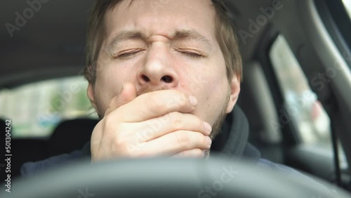Close up portrait sleepy young man driver yawning on the front seat of the car. photo