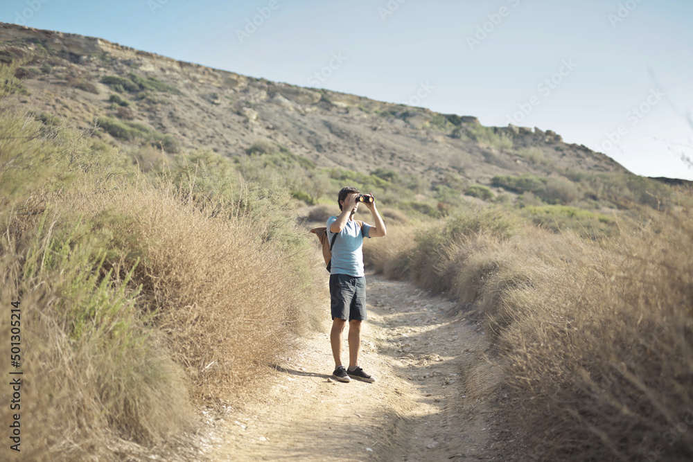 young man with backpack looks the way with binoculars
