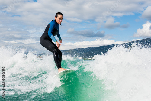 Athletic woman in wetsuit riding on endless waves behind a boat on sunny day. Female learning wakesurfing and perfecting tricks. Watersport concept.