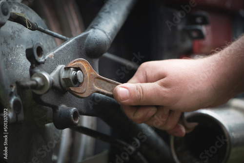 Biker unscrews a motorcycle wheel with a wrench close-up.